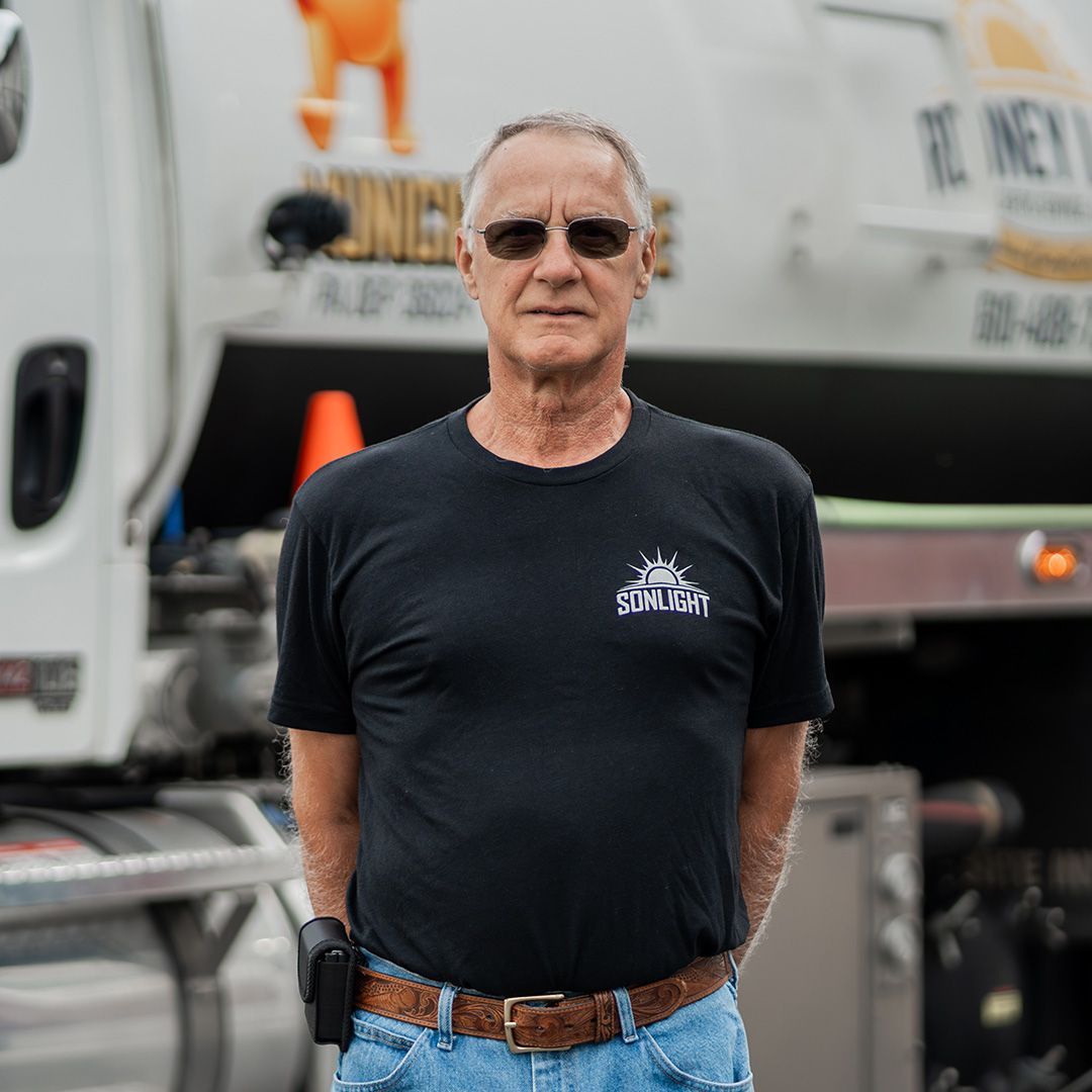 Robney standing in front of a white truck, wearing sunglasses, a black T-shirt, and gloves