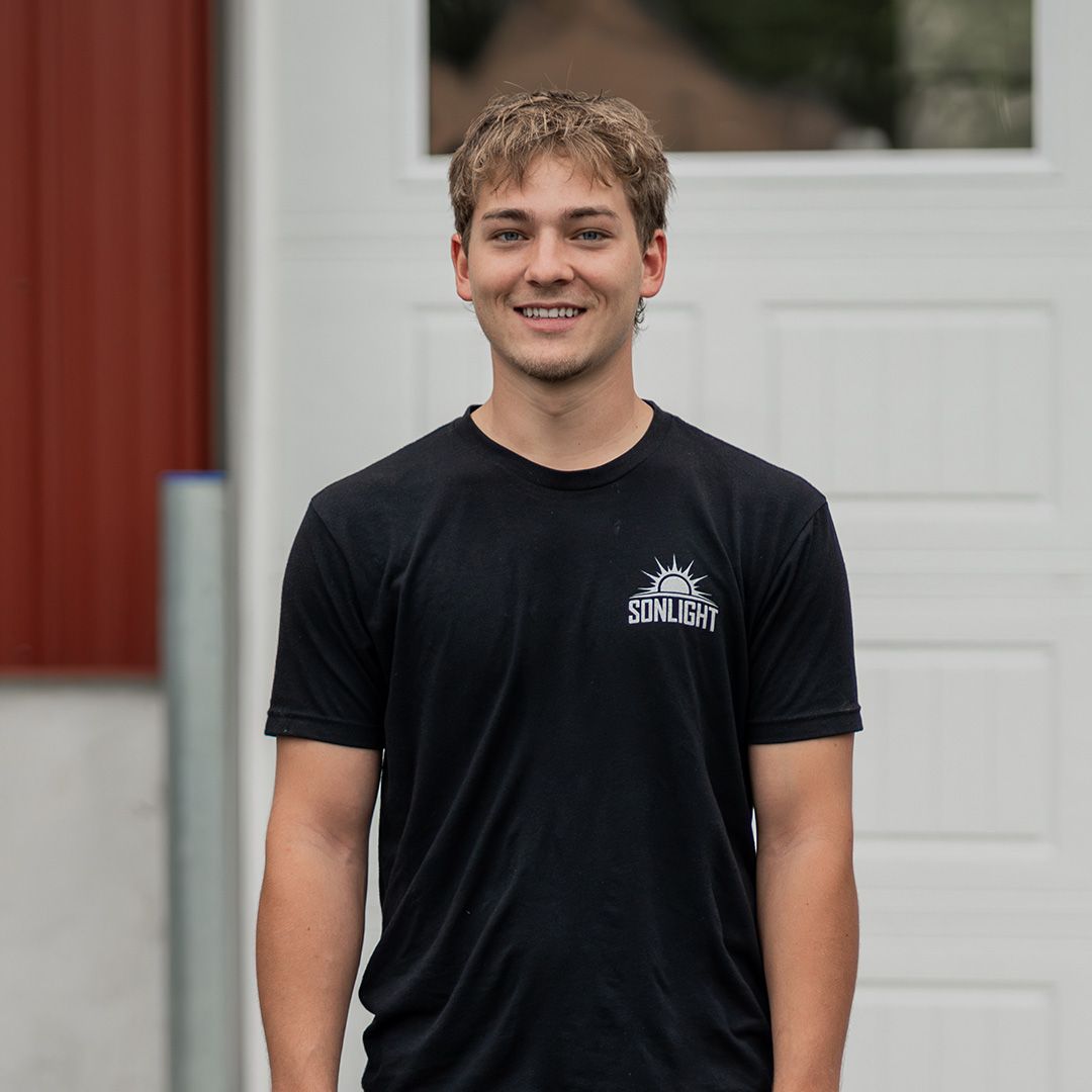 Skylar in glasses wearing a black T-shirt, standing in front of a white truck outdoors.