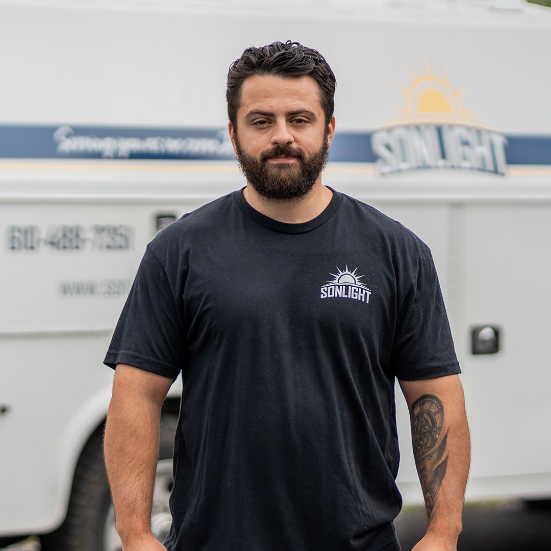 Thomas standing in front of a white service truck, wearing a black T-shirt and looking at the camera.