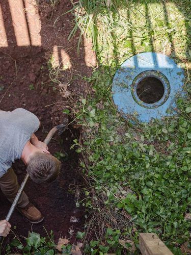 Person using a hose to water a garden beside a blue circular well cover