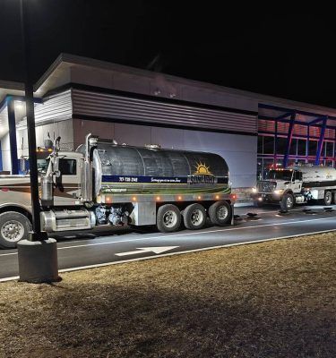 Nighttime scene with two parked semi-trucks beside a building, one tanker truck in the foreground.