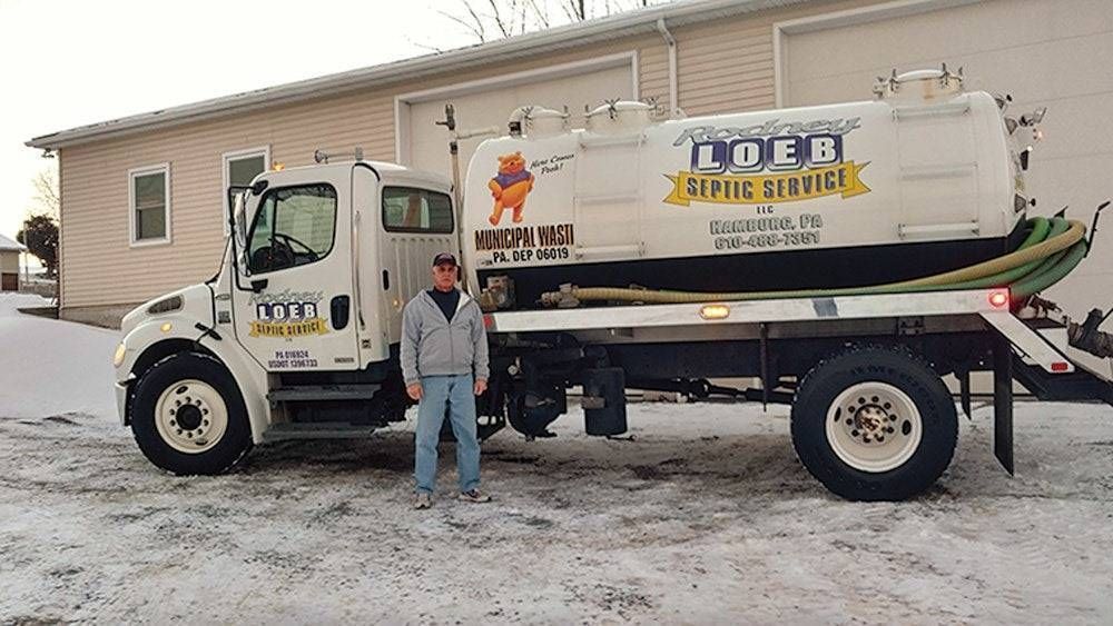 Tow truck with “TOW” branding parked in snow beside a person and a house