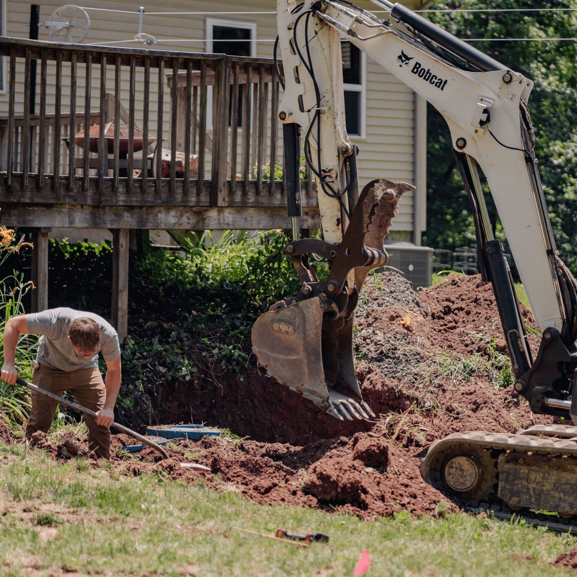 Worker beside excavator digging brown soil near a blue manhole cover