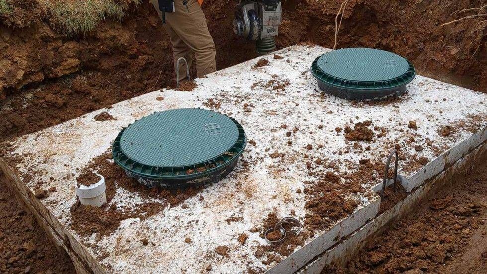 Two green septic tank lids on a concrete slab in a muddy excavation site