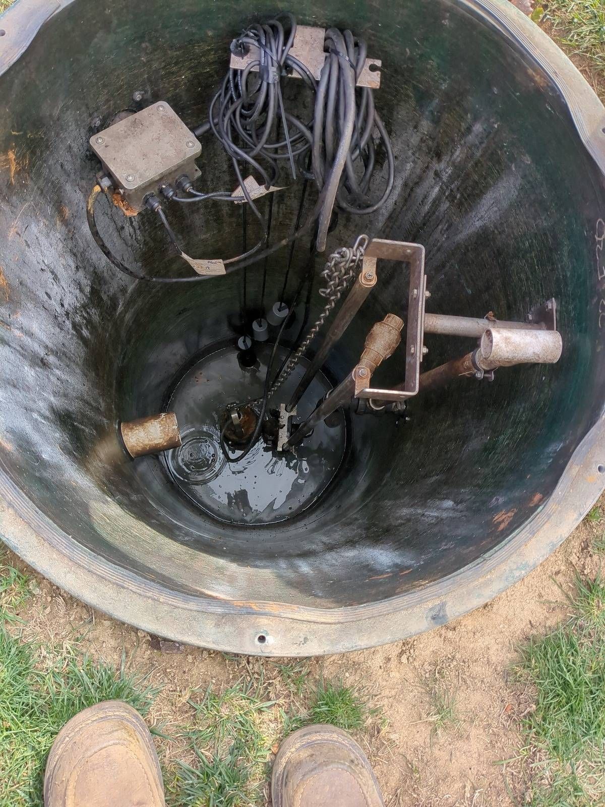 Open utility well with cables, pipes, and a submerged valve assembly.