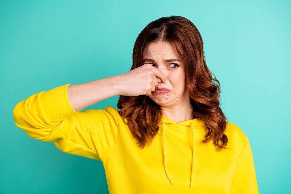 Woman in yellow sweater pinching her nose, looking disgusted against a turquoise background