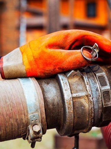 Orange work glove on a metal fire hose coupling with a blurred industrial background
