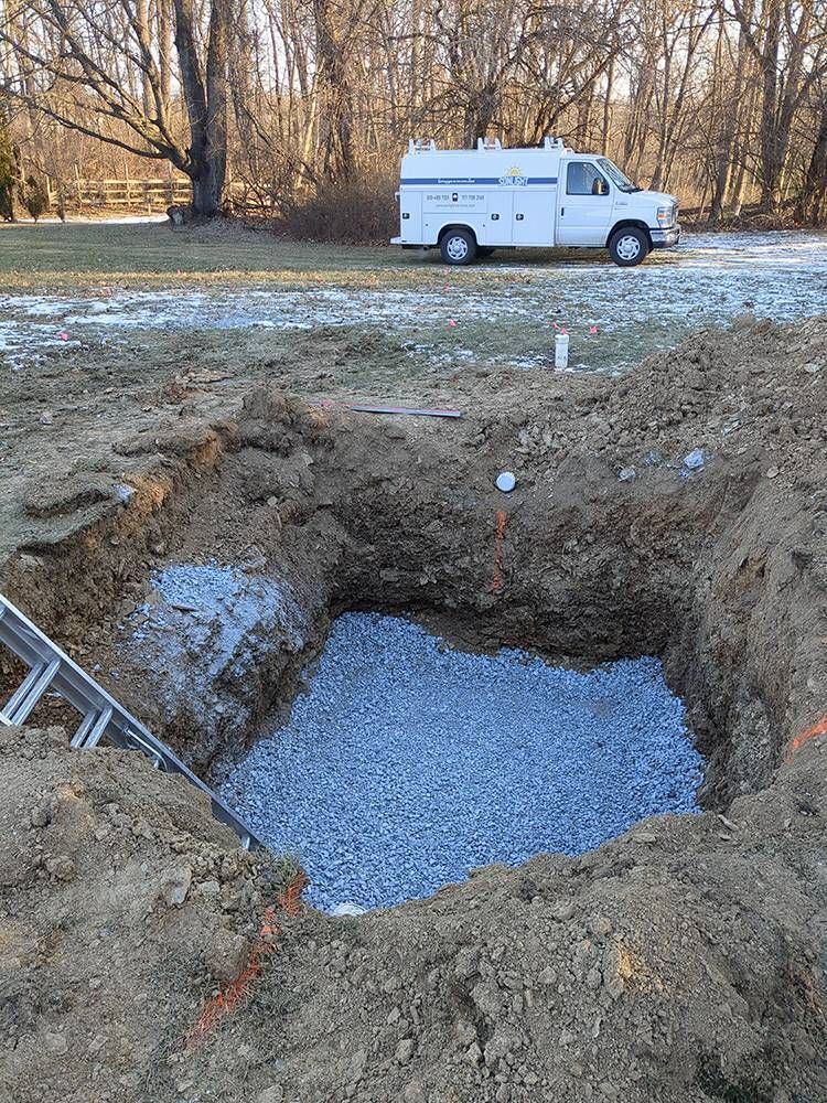 Excavation pit filled with gravel and dirt, with a white van parked in the background.