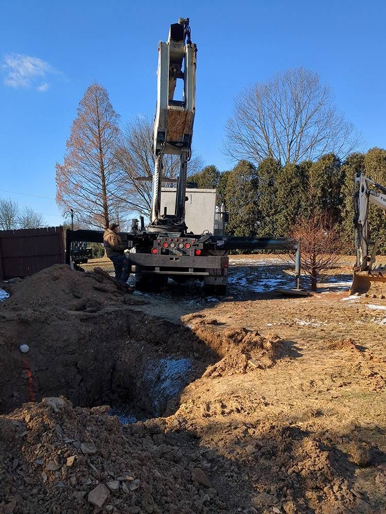Excavator at a construction site beside a large dirt trench under a clear blue sky