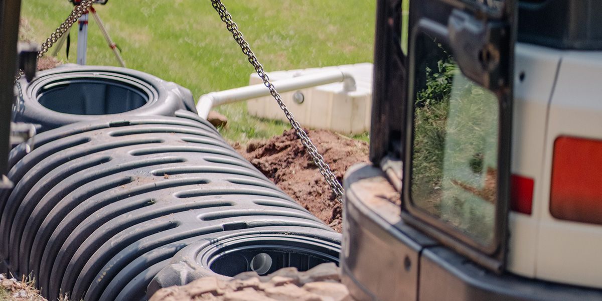 Excavator lifting a large corrugated drainage pipe at a construction site.
