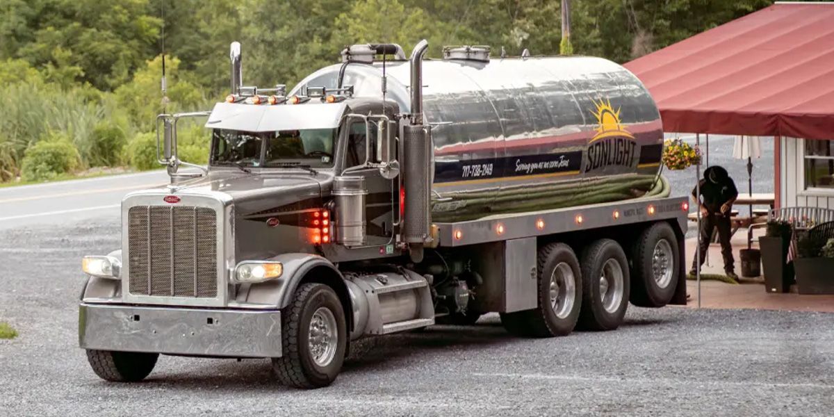 Silver tanker truck parked beside a red-roofed shelter on a roadside.
