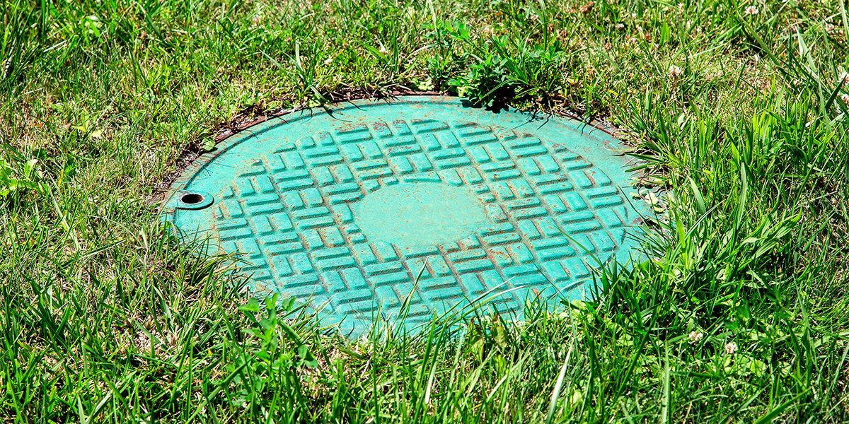 Green utility cover in grass with a turquoise circular lid and a small hole on the left
