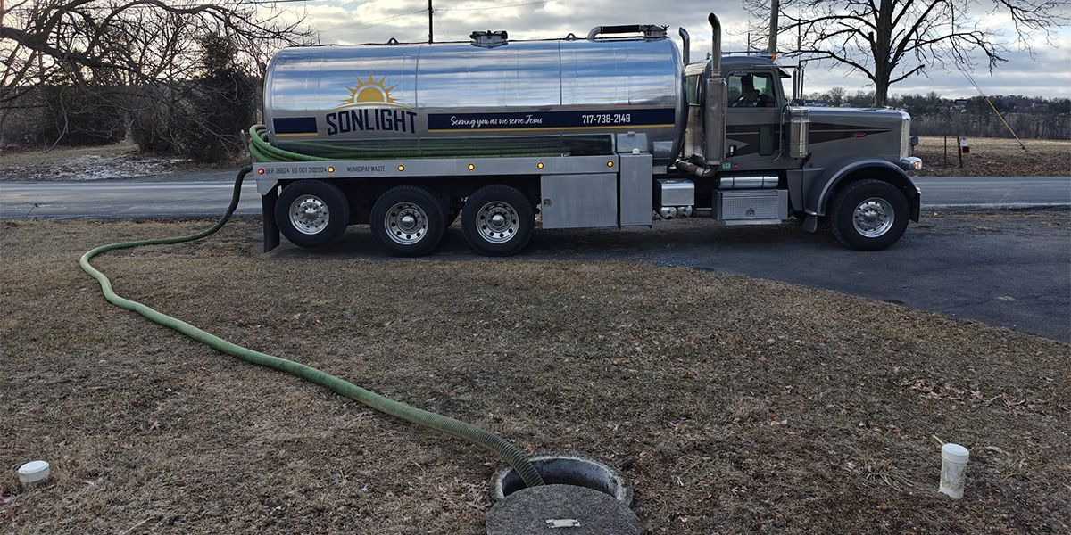 Silver tanker truck with hose on gravel roadside near open field