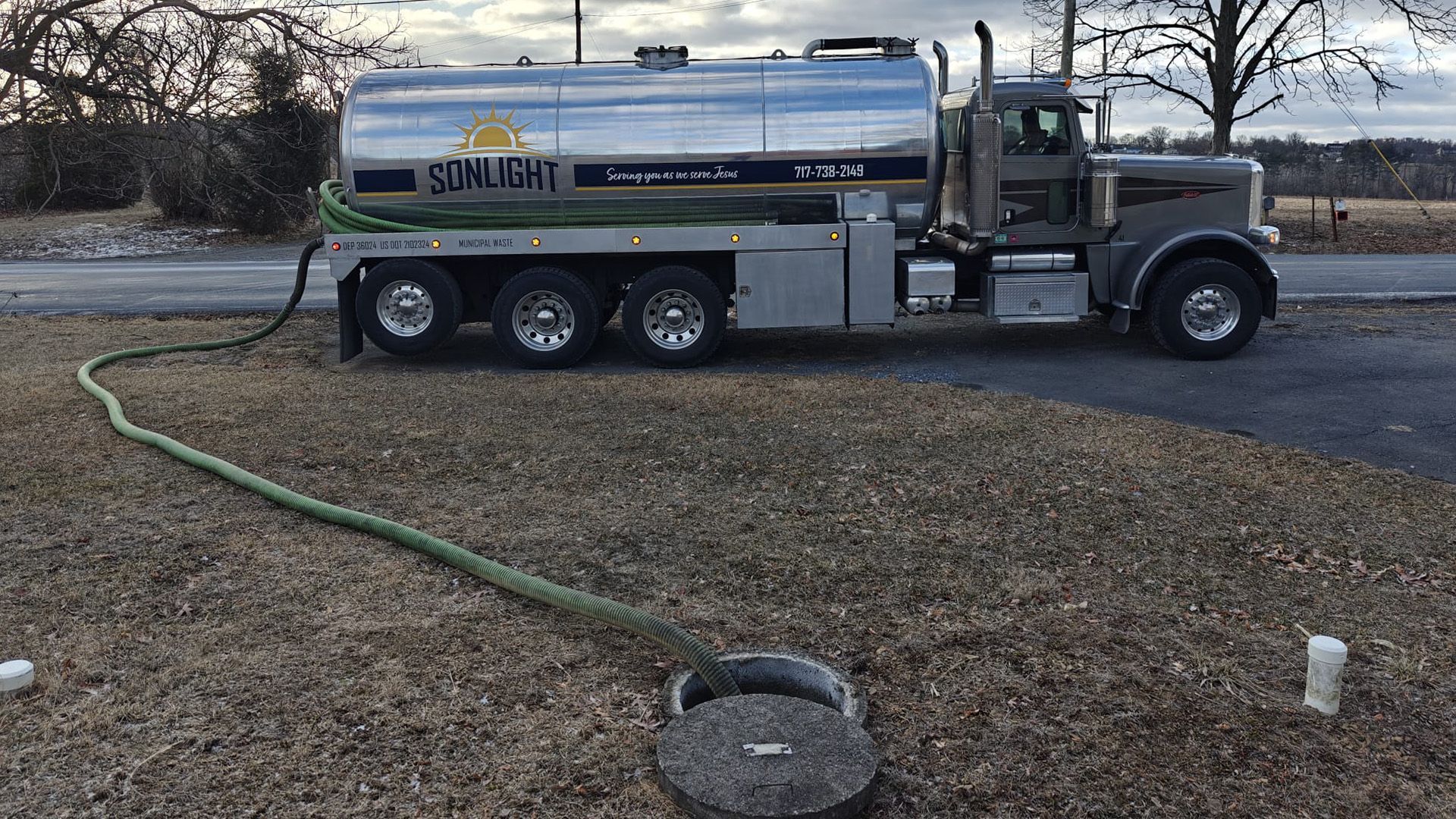 Silver water tanker truck parked on grass, with hose stretched to a ground opening