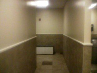 Narrow indoor hallway with beige walls, brown wainscoting, and a white box at the far end.