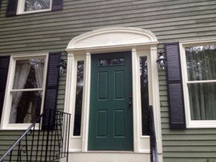 Front door with green door, white columns, and black shutters on a house exterior