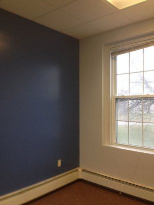 Empty room with blue wall, white trim, and a window letting in daylight.