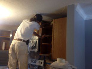 Person standing on a step stool, reaching into a tall kitchen cabinet
