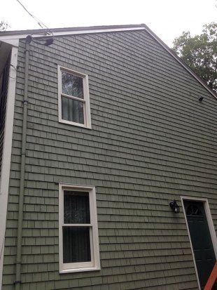 Gray shingled house exterior with two windows and a dark front door