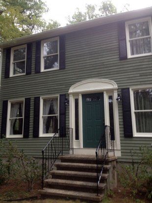 Two-story green house with black shutters, white trim, and a front porch with steps and railings