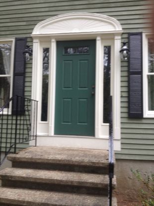 Front entrance with green door, white trim, and black shutters above stone steps.
