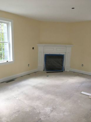 Empty beige room with white fireplace, single window, and bare floor under renovation
