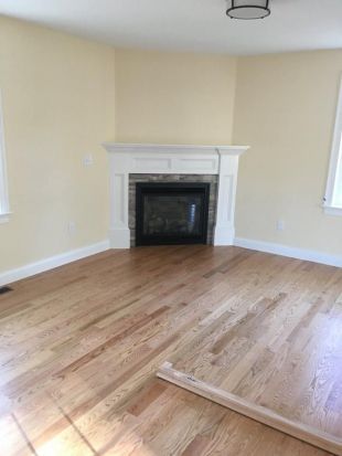 Empty living room with hardwood floors and a white fireplace.