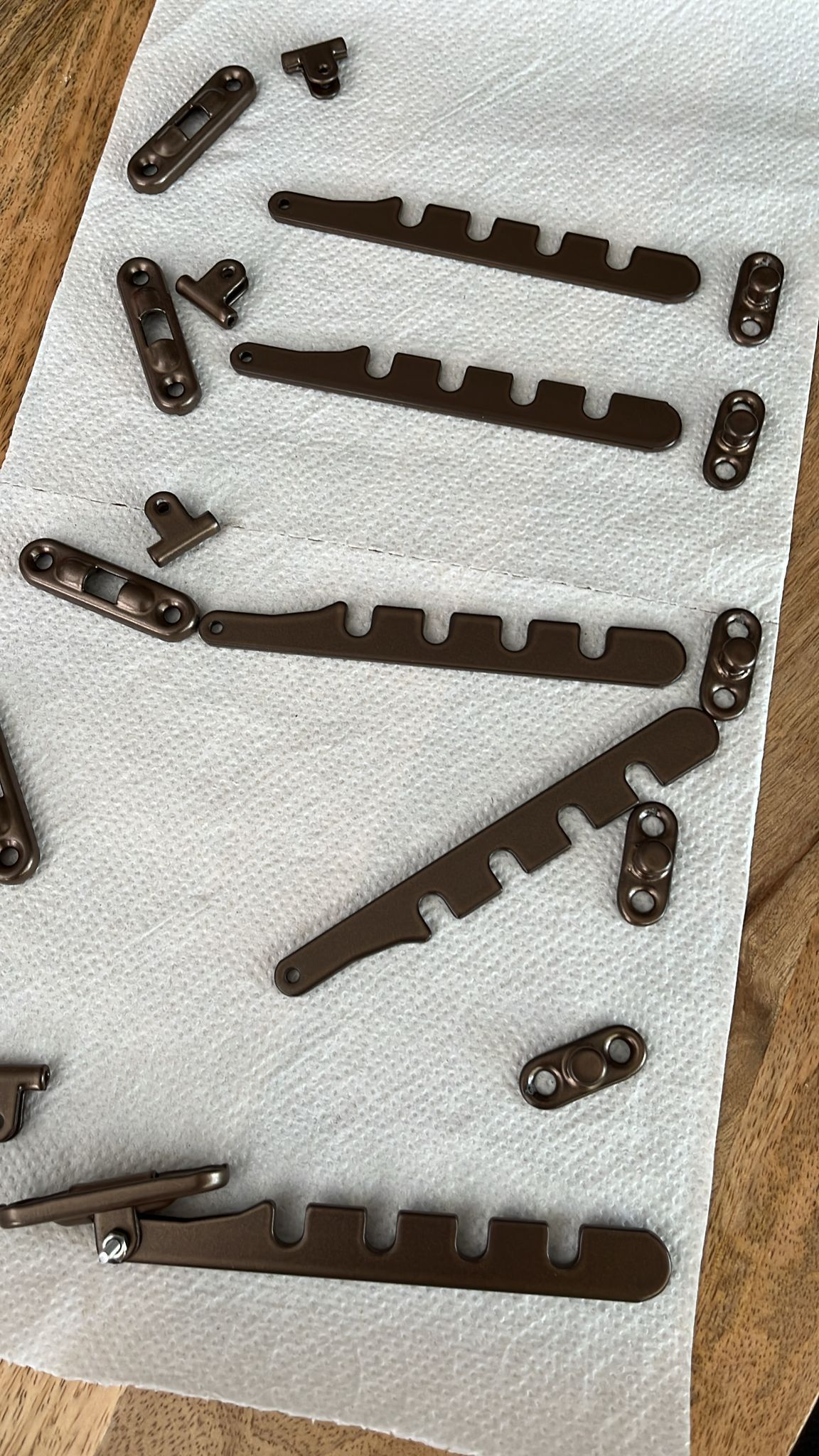 Diverse donkere metalen onderdelen en schroeven uitgestald op een witte stoffen ondergrond.