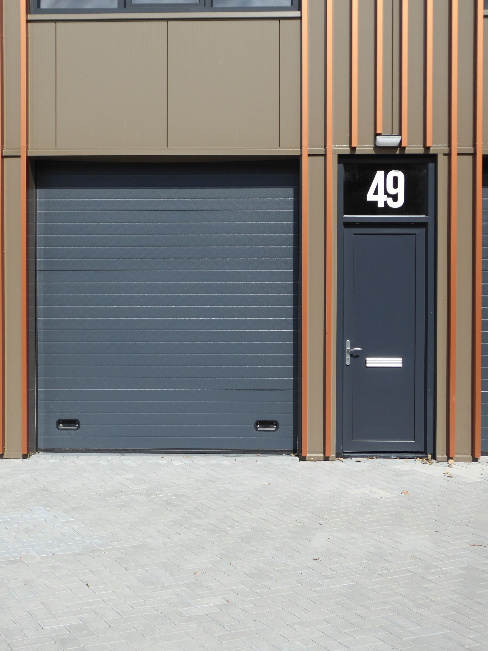 Industriële gebouwgevel met grijze garagedeur en donkere toegangsdeur, gemarkeerd met 49.