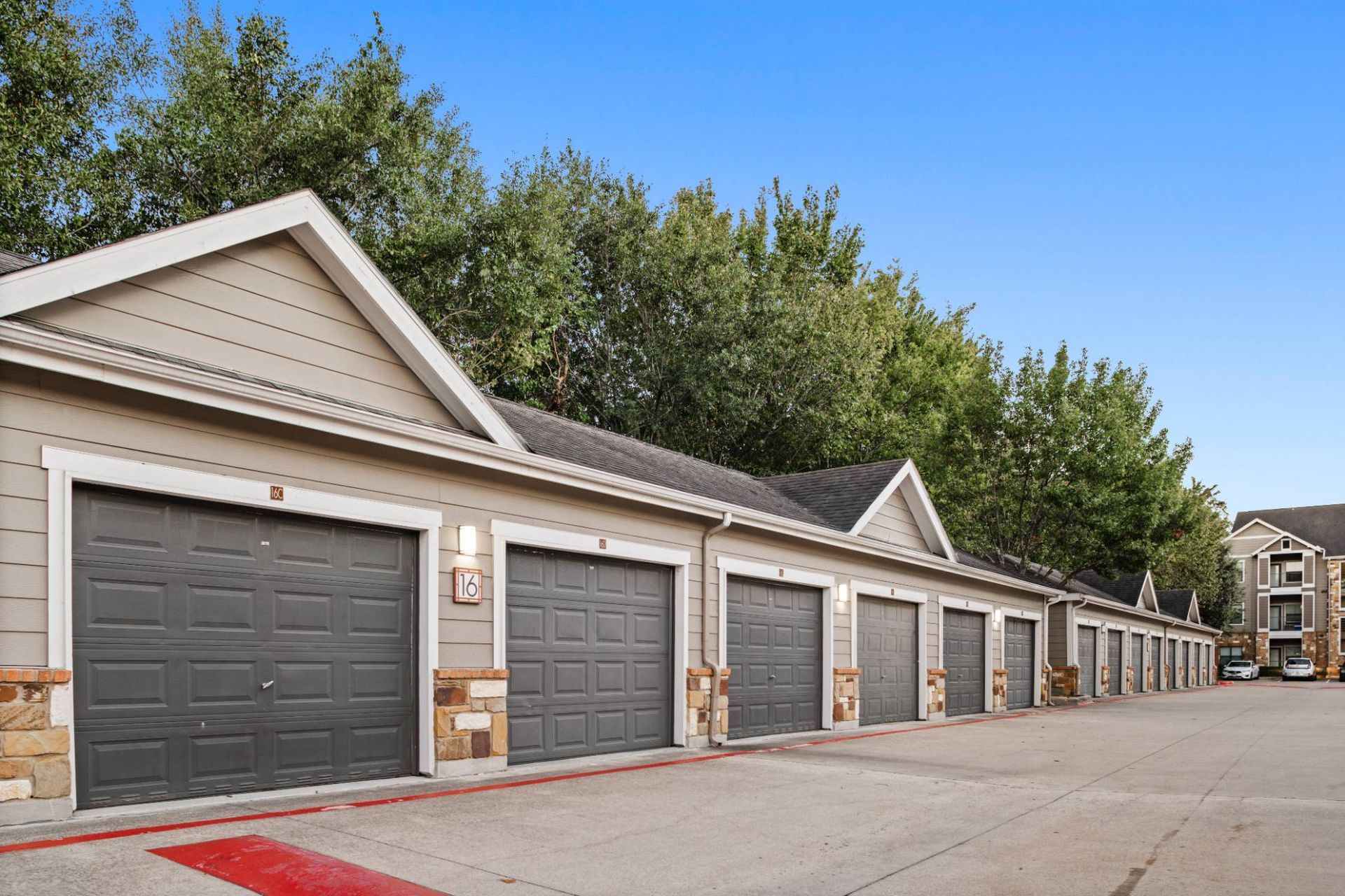 Row of beige garage doors at a residential complex, with trees and blue sky.