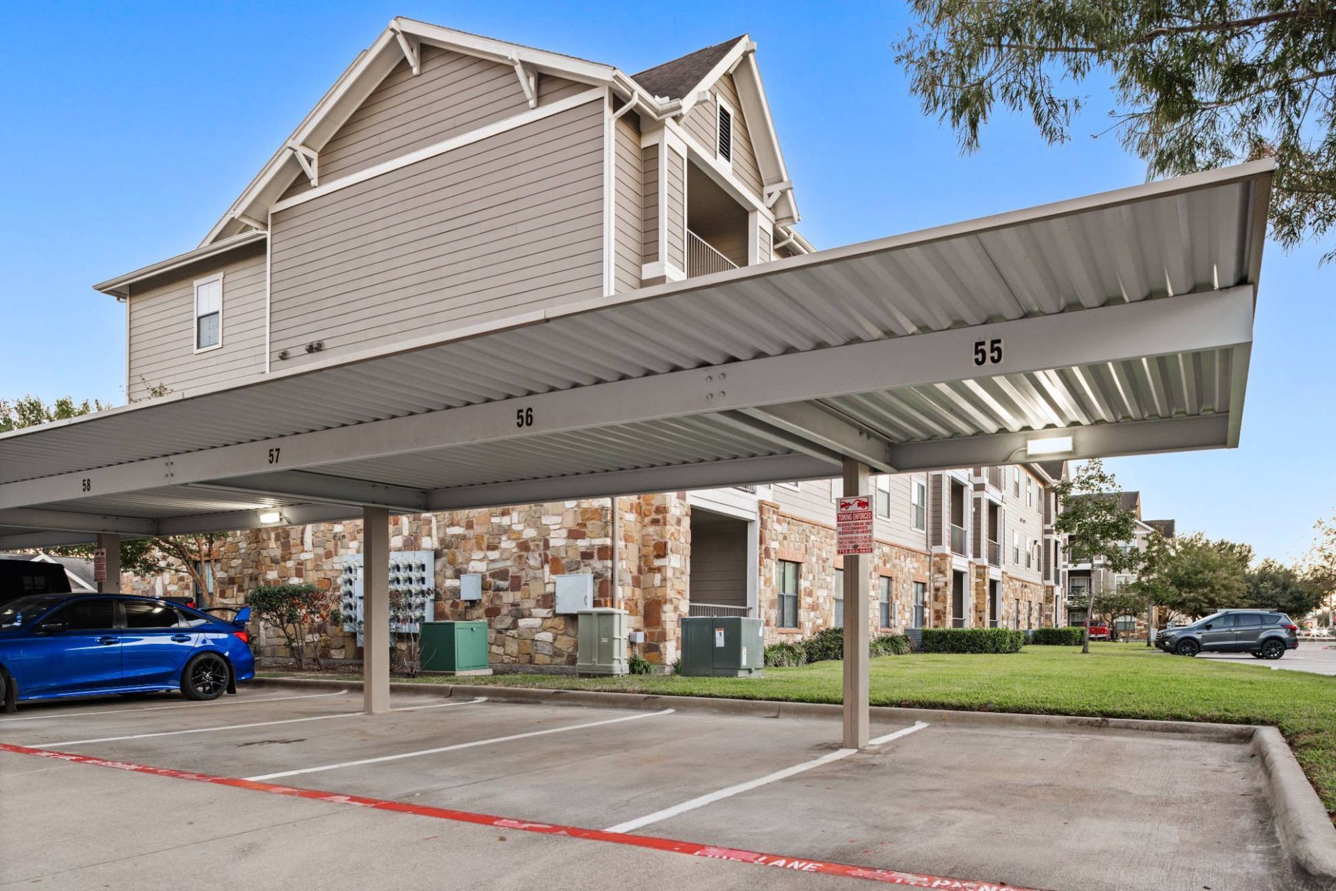 Covered parking with numbered bays 56–58 beside a multi-family building.