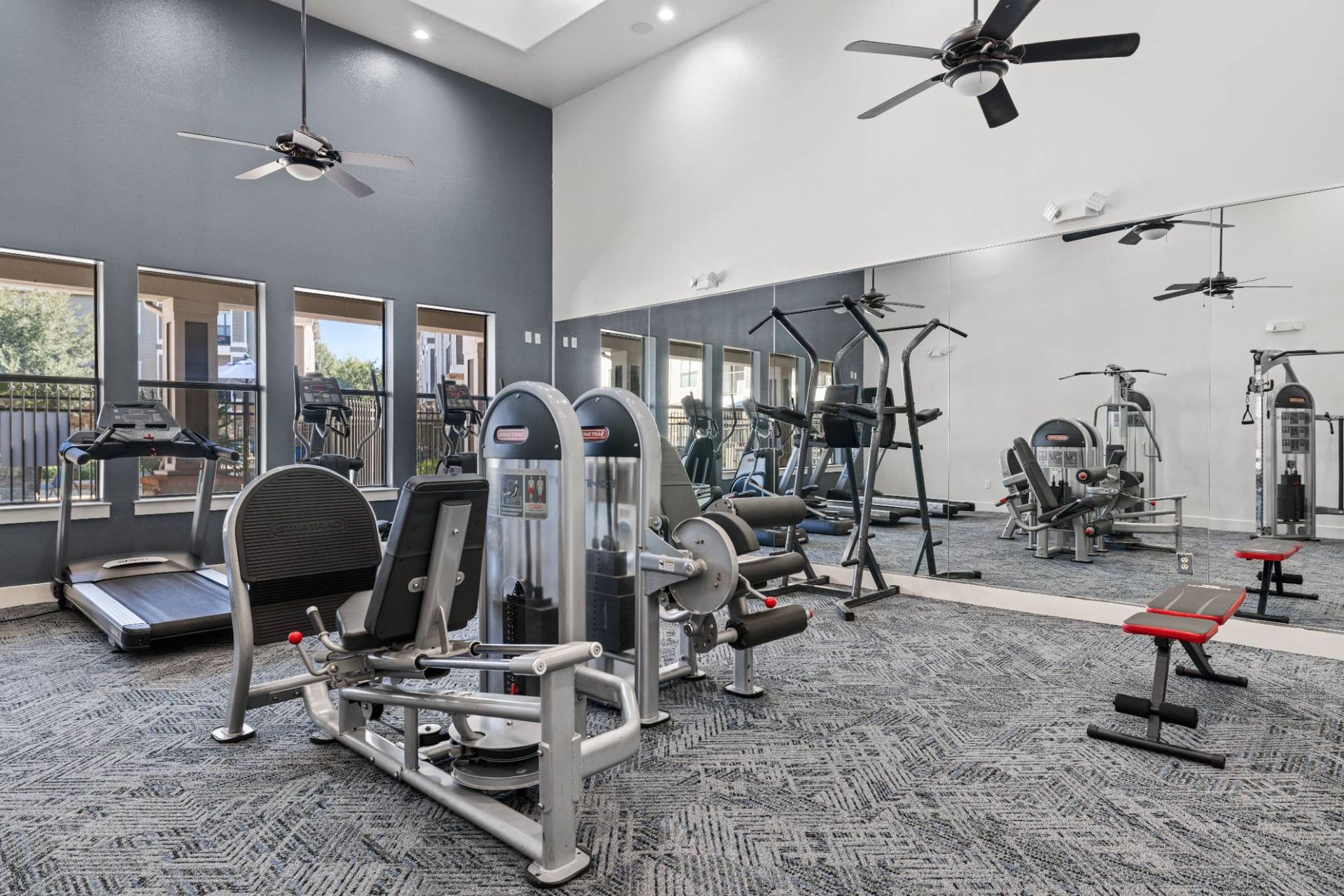 Interior view of a communal apartment gym with cardio and strength equipment and mirrors.