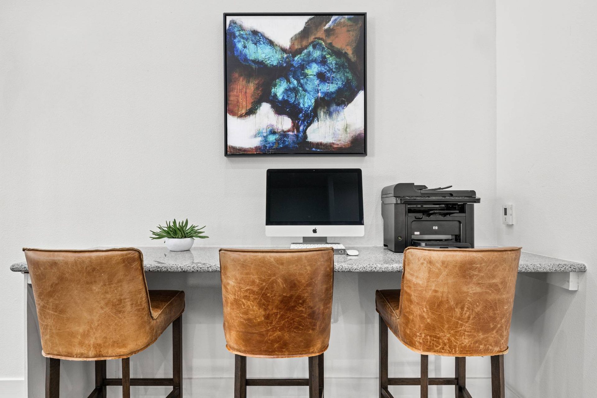 Apartment workstation with a granite desk, iMac, printer, plant, and abstract wall art.