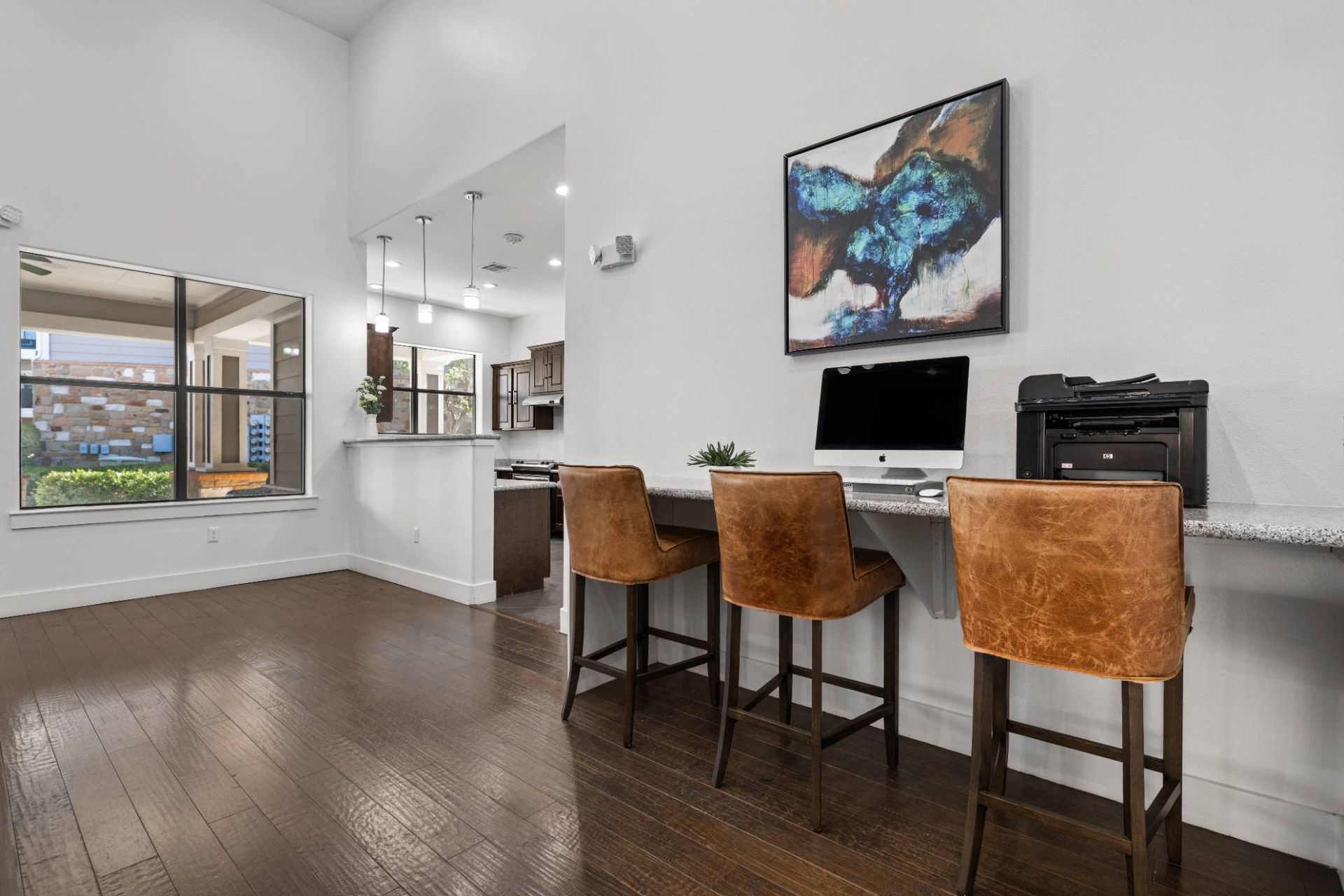 Leasing office/common area with computer station, printer, and three brown leather chairs along a counter.