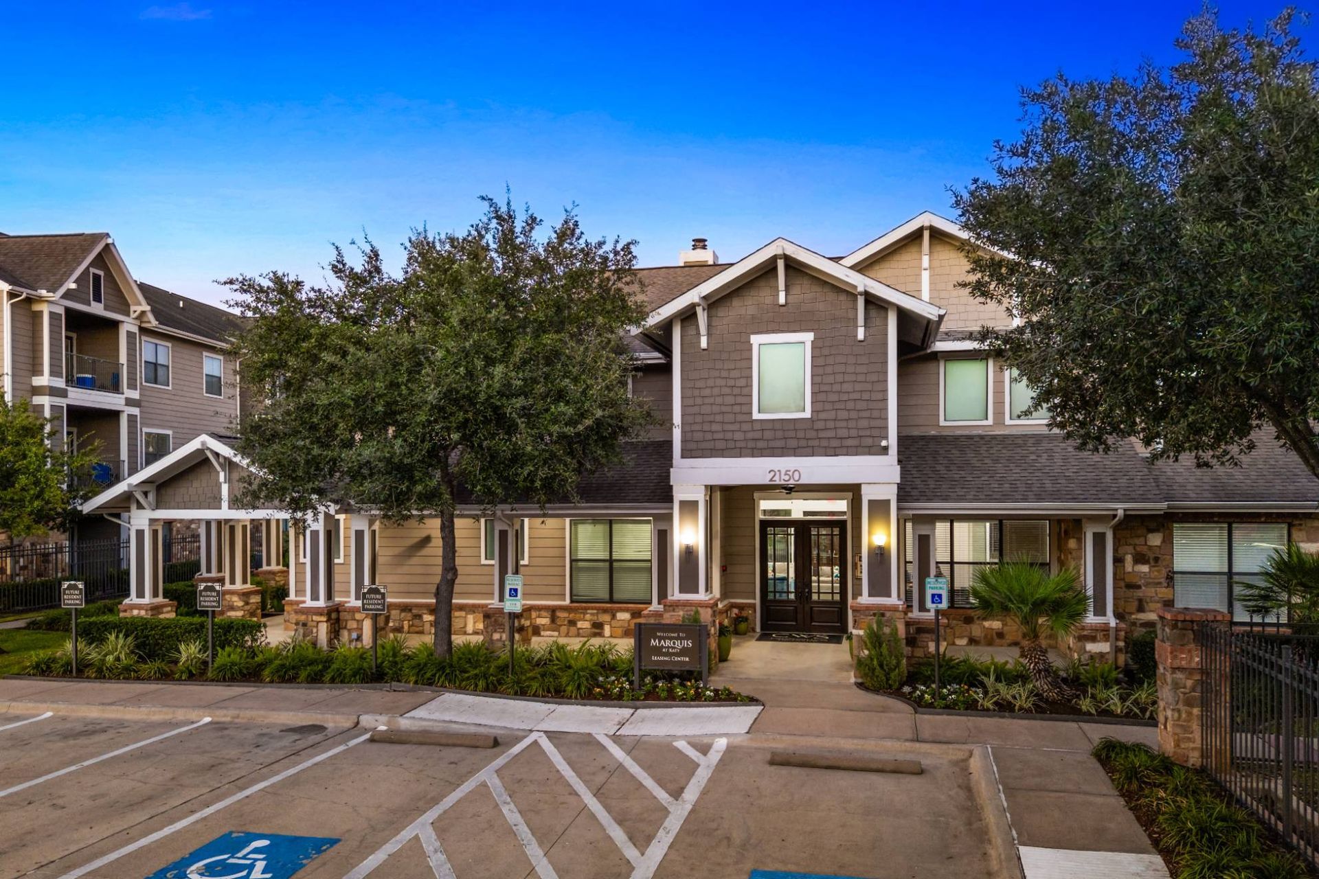 Exterior view of a modern apartment complex with a central entrance, parking, and landscaping.