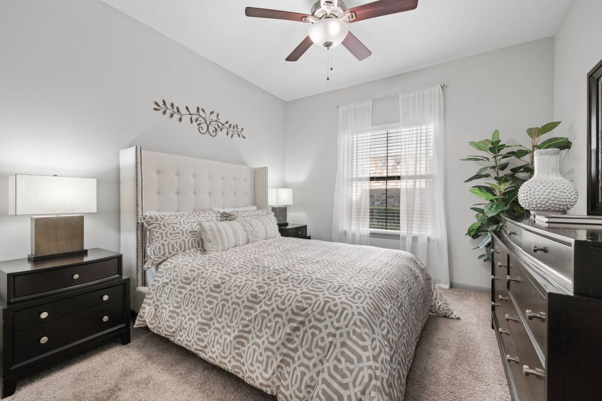 Bedroom with a tufted headboard, white curtains, two dark nightstands, and a dresser.