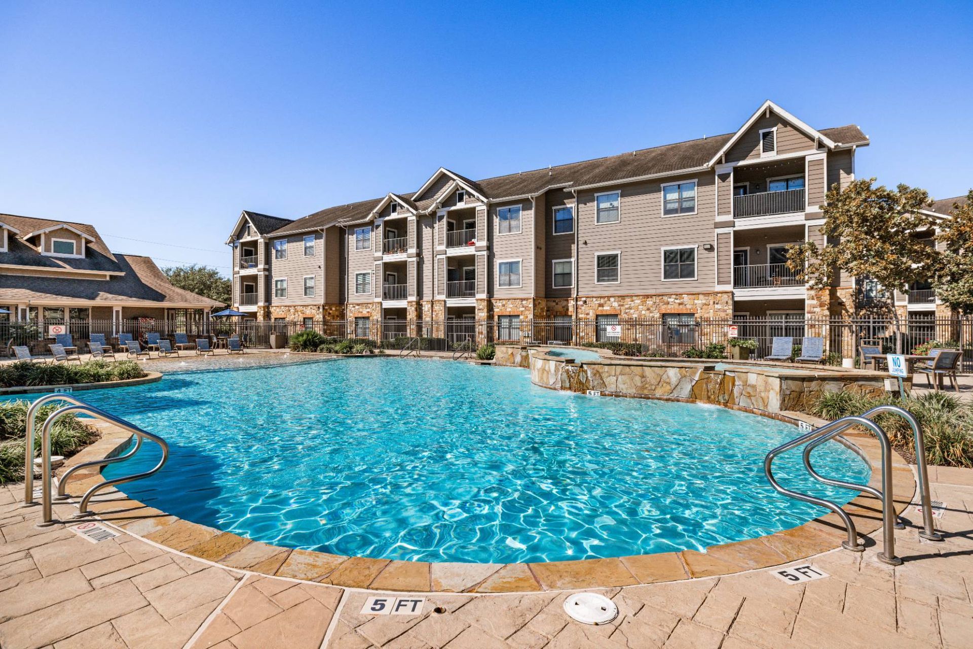 Outdoor pool surrounded by lounge chairs and apartment buildings.