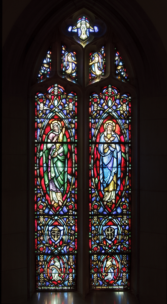 Stained-glass window depicting two figures with intricate colorful details in a dark setting.