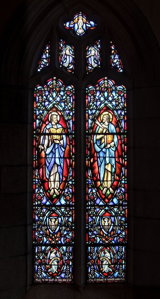 Stained-glass window featuring two figures in blue and yellow robes, surrounded by floral patterns in red, blue, and green.