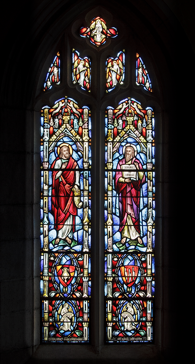 Stained-glass window with two figures in red robes; blue and white details, gothic arches, and colorful scenes above.