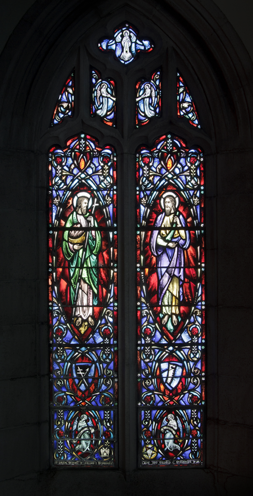 Stained-glass window with two figures in green and purple robes, surrounded by ornate blue and red floral designs.