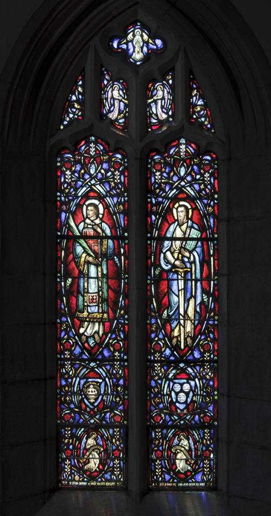 Stained glass window depicting two figures within intricate red, blue, and white floral designs, set in a church.