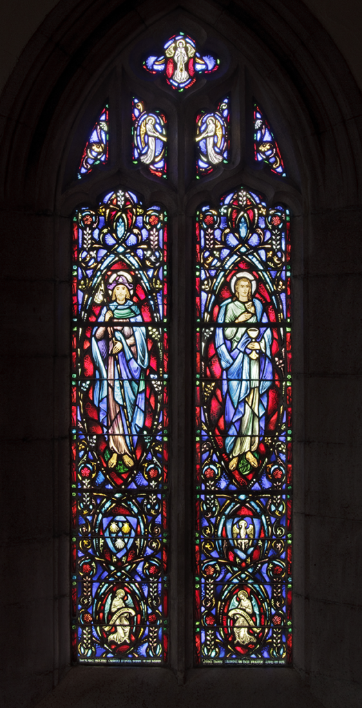 Stained glass window with two figures in blue robes, surrounded by colorful floral patterns, in an arched setting.