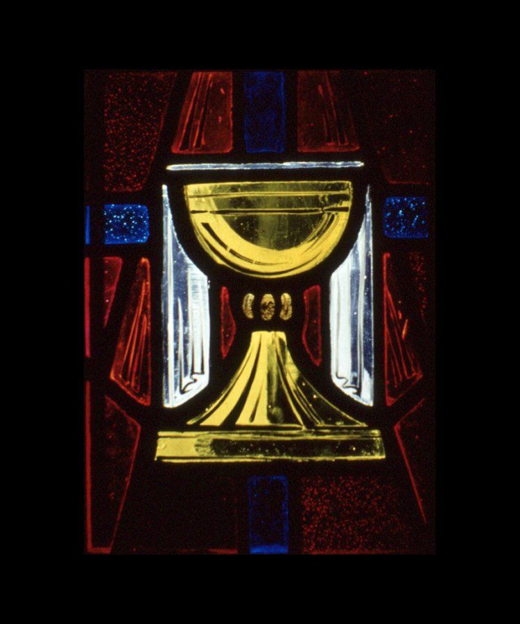 Stained-glass chalice, yellow with gold trim, against a backdrop of red, blue, and white glass.