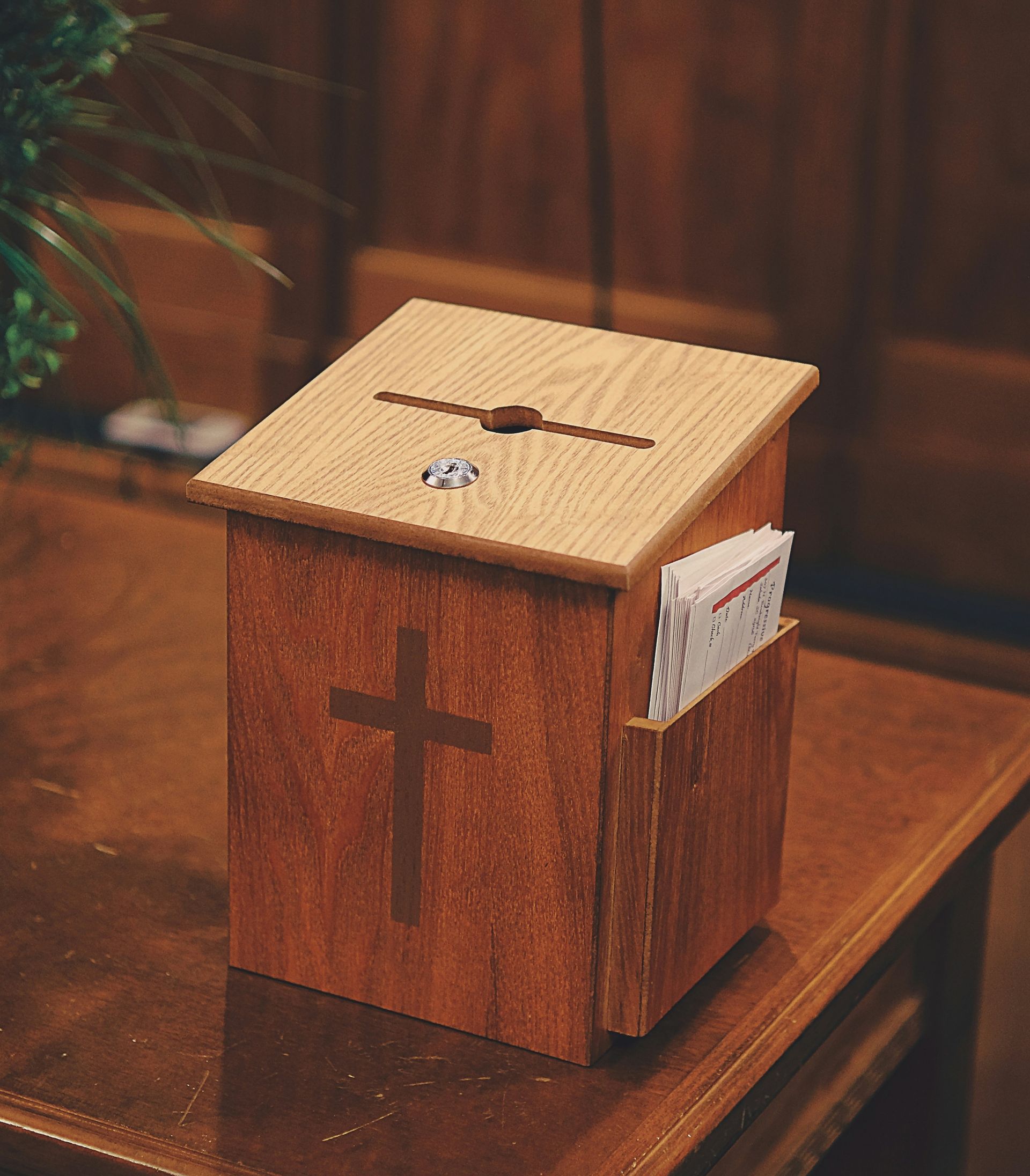 Wooden donation box with cross on it, leaflets in side pocket, on wooden table.