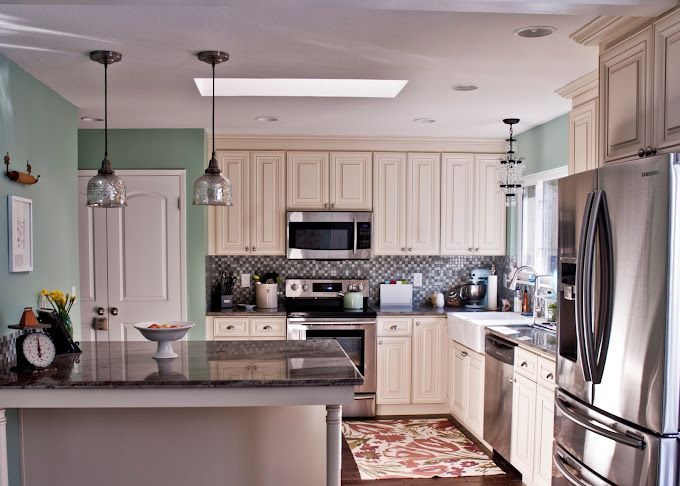Bright, modern kitchen with white cabinets, stainless-steel appliances, dark island, and green walls