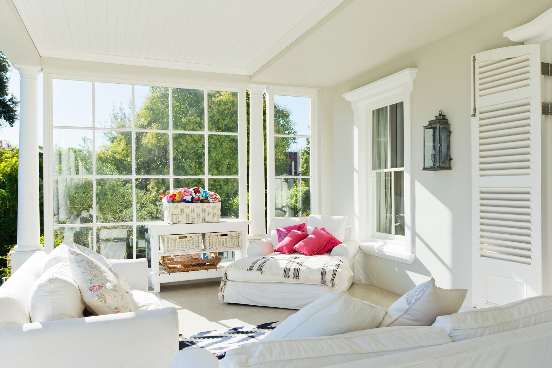 Bright, airy sunroom featuring white sofas, a matching console table, and pink decorative pillows.