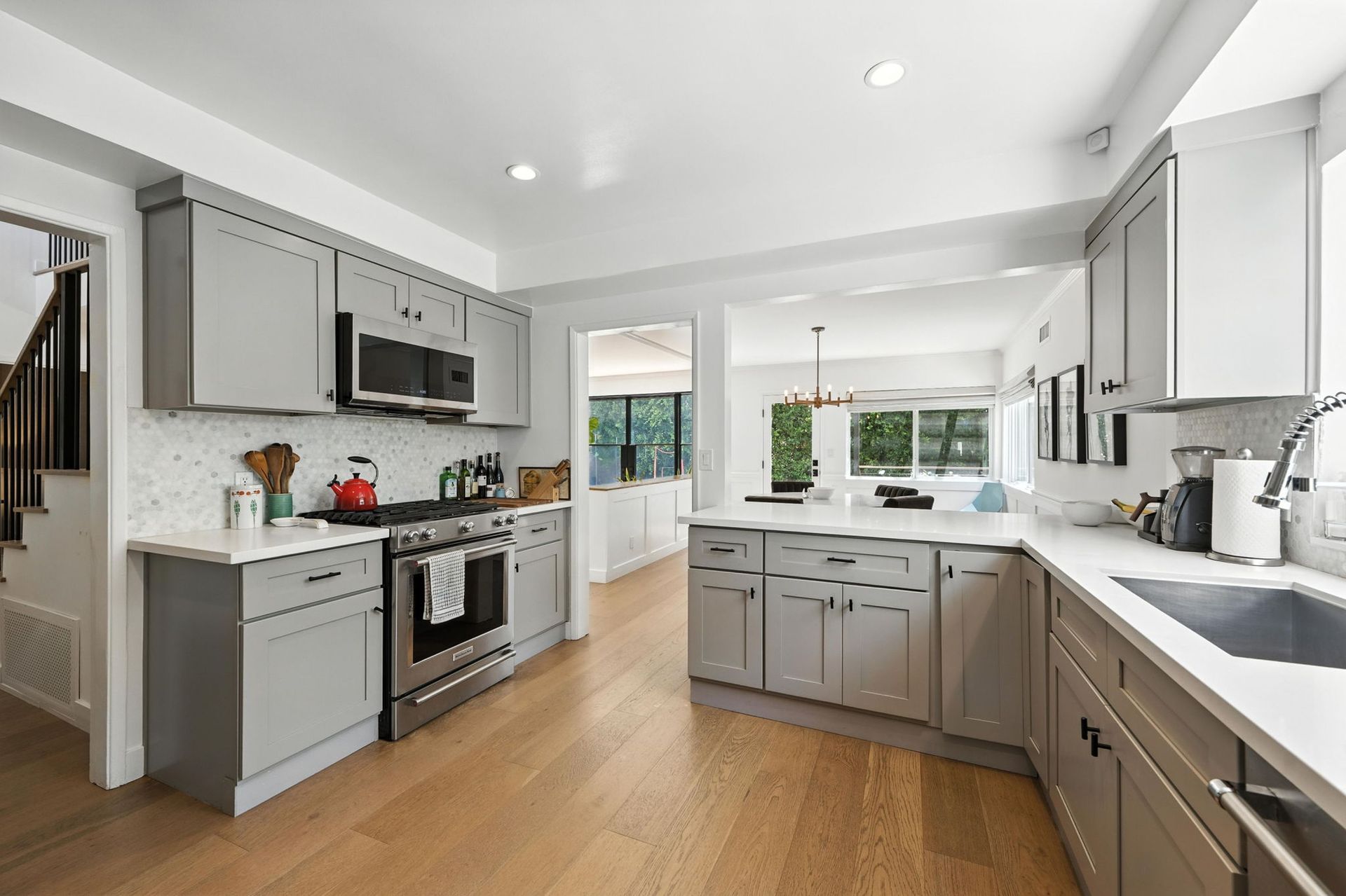 A kitchen with light gray cabinets, white countertops, stainless steel appliances, and light wood flooring.