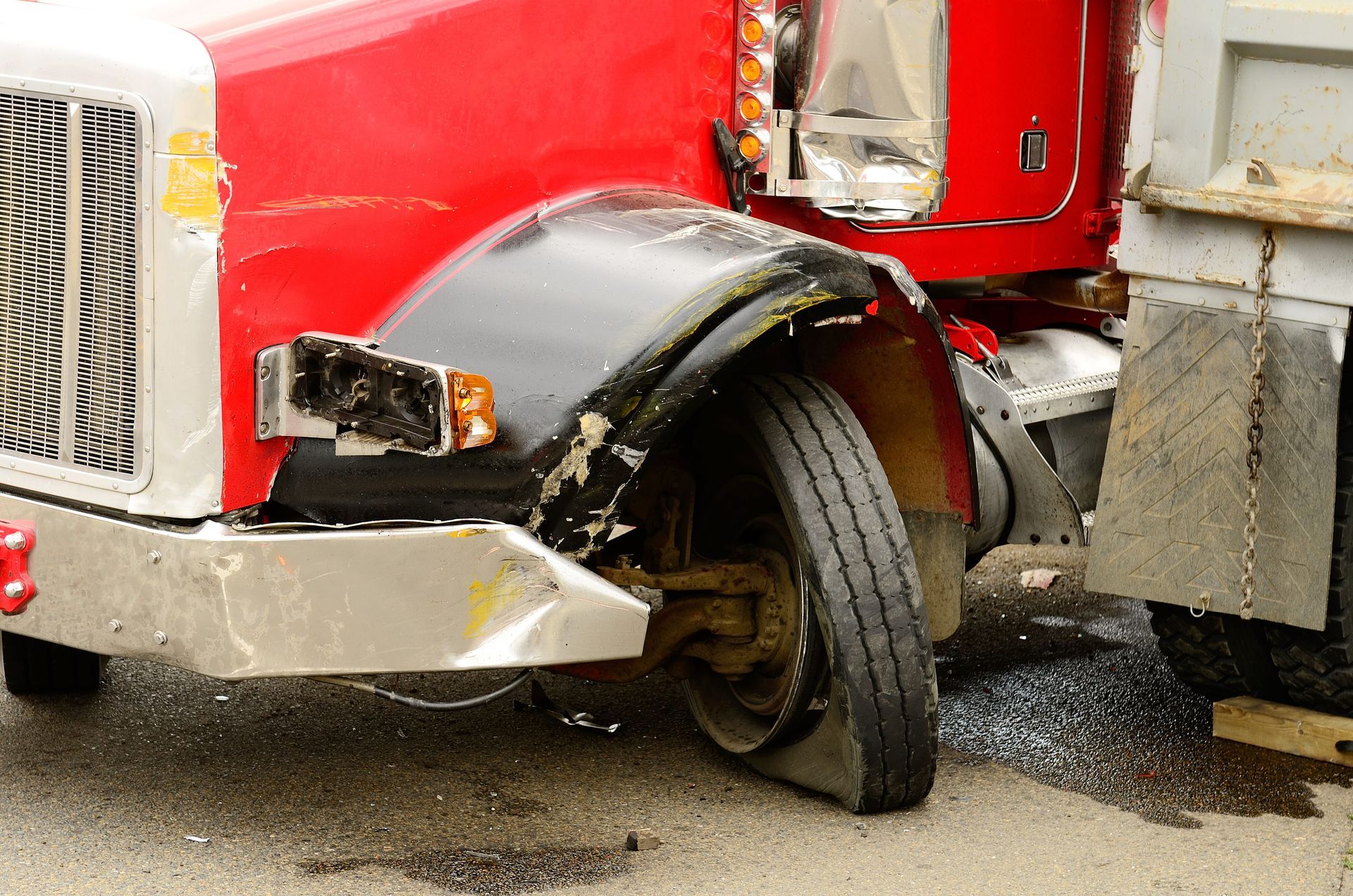 Red truck with a damaged front wheel and bent fender after a collision.