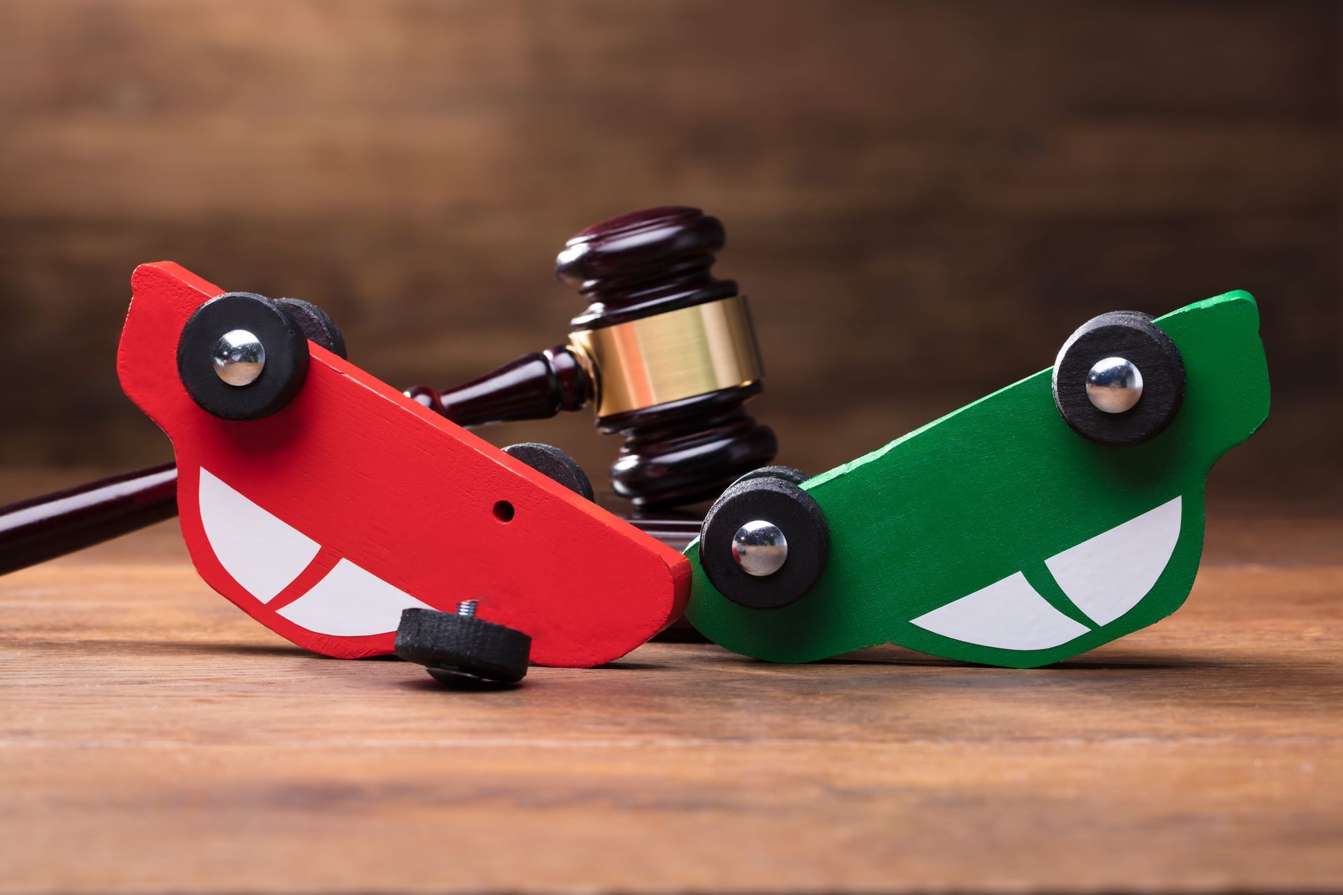 Red and green mechanical toy cars colliding on a wooden surface, with a gavel-like piece between them.